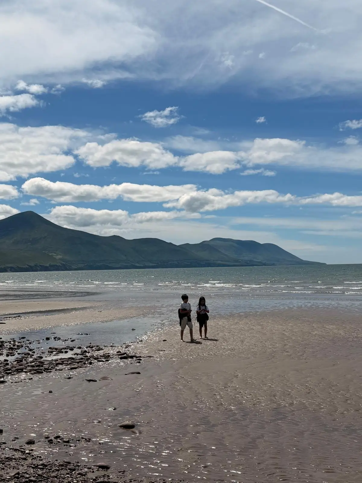 Two people walking on Rossbeigh Beach in Ireland beneath a blue sky